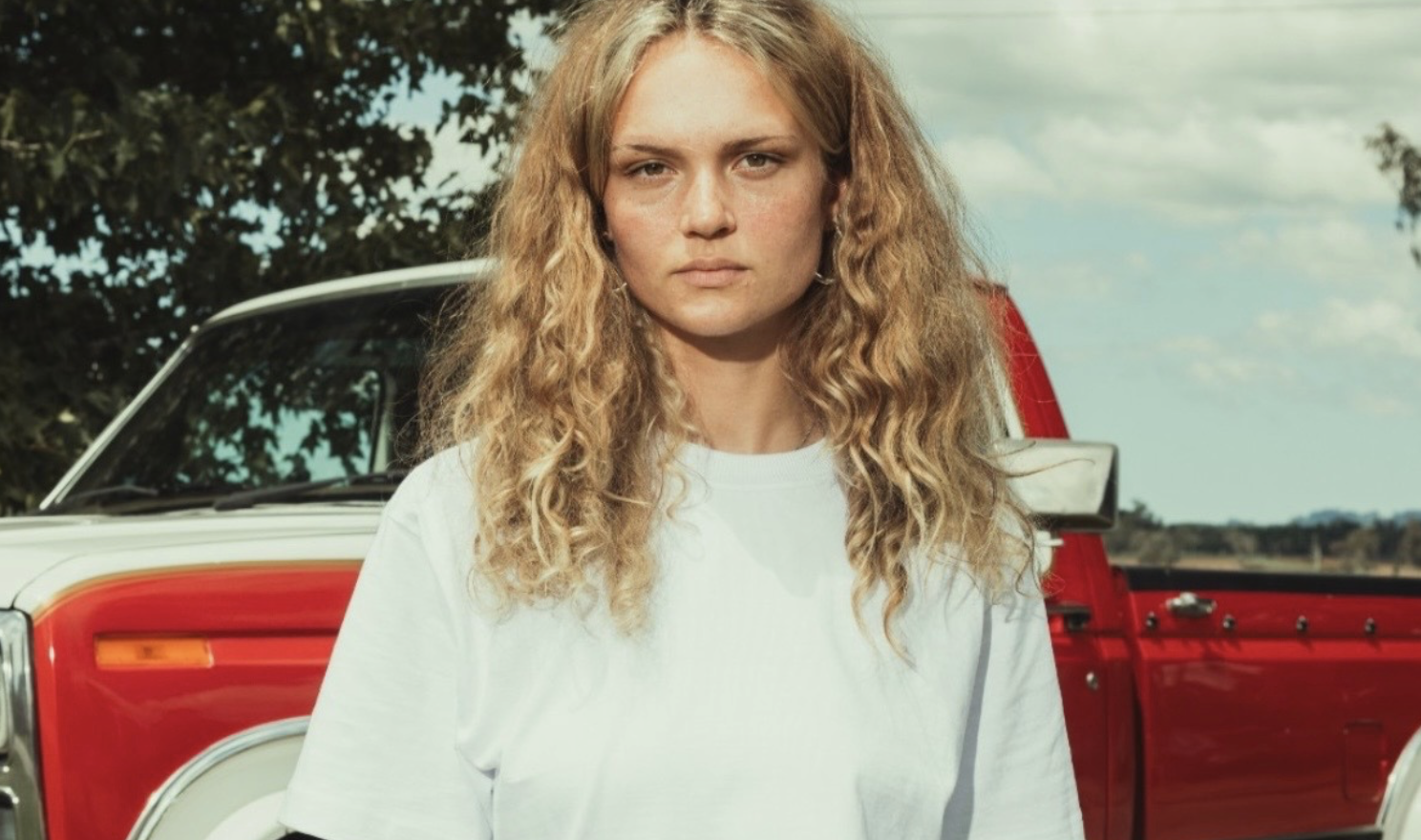 American Apparel 9001 Super Heavyweight Tee in white, styled outdoors in front of a red vintage pickup truck.